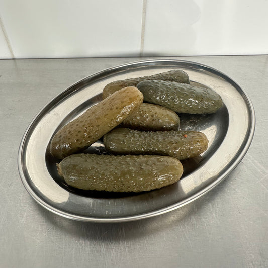 Cornichons on a metal tray with a tiled wall background