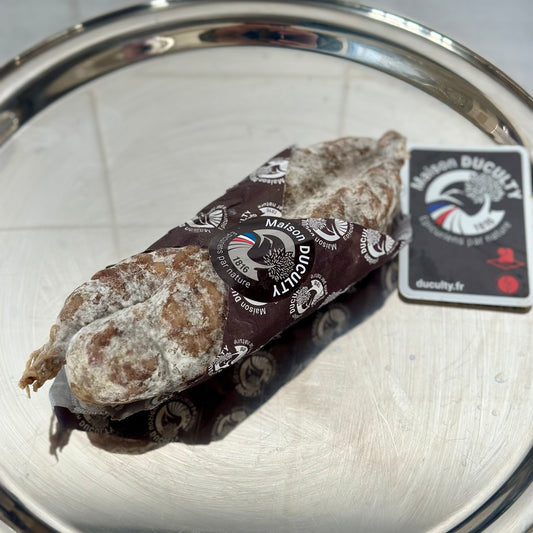 Saucisson with a Duculty paper wrap on a metal surface.