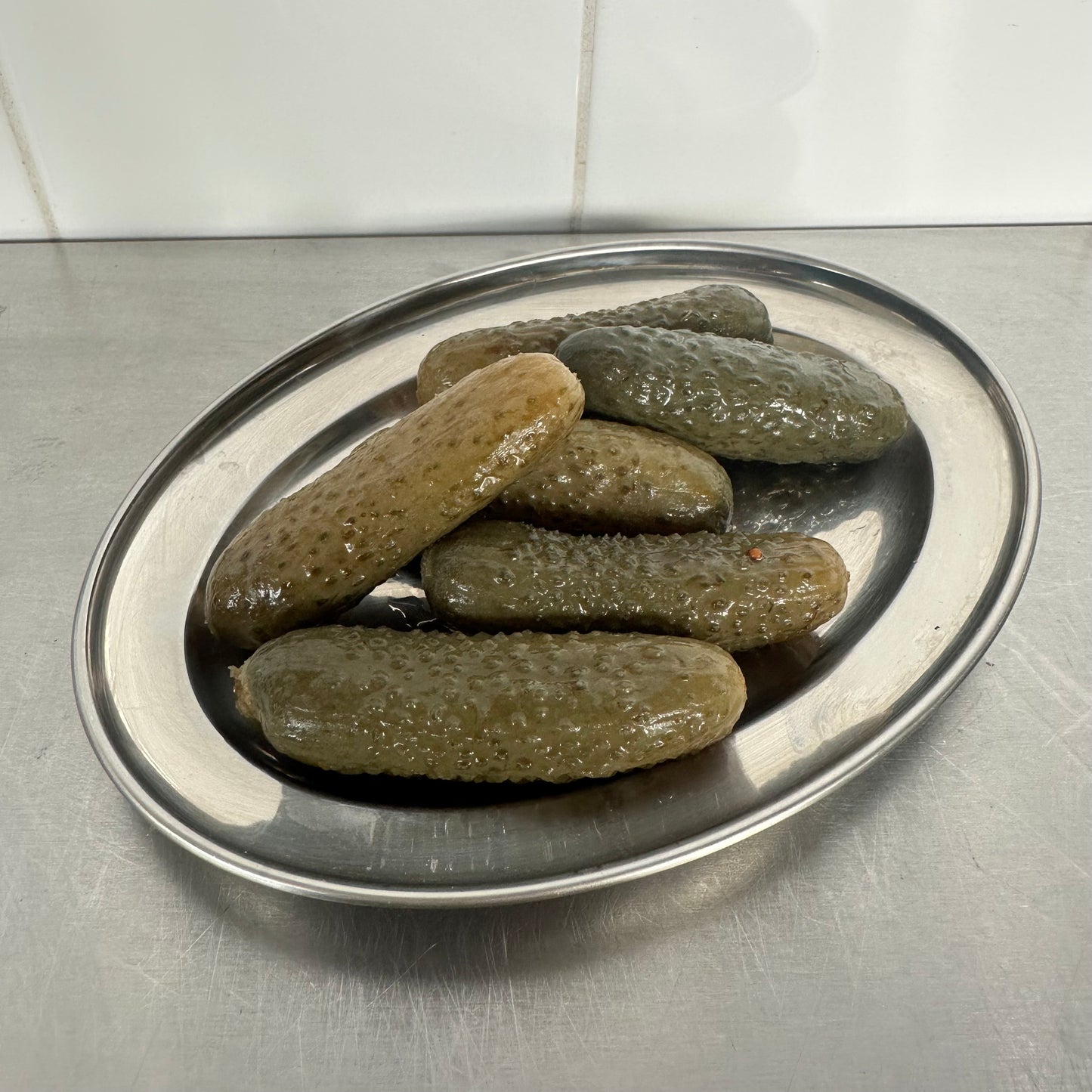 Cornichons on a metal tray with a tiled wall background