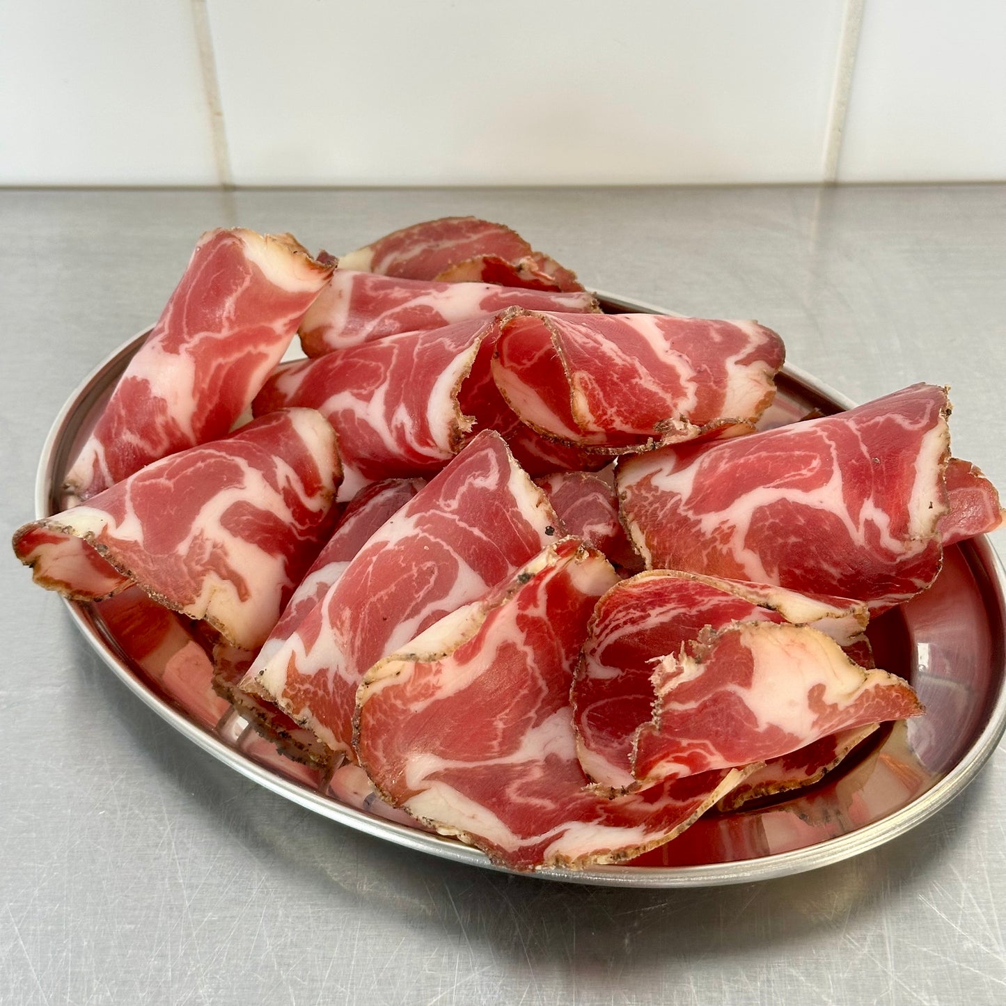 Sliced Coppa on a metal plate with a tiled wall background