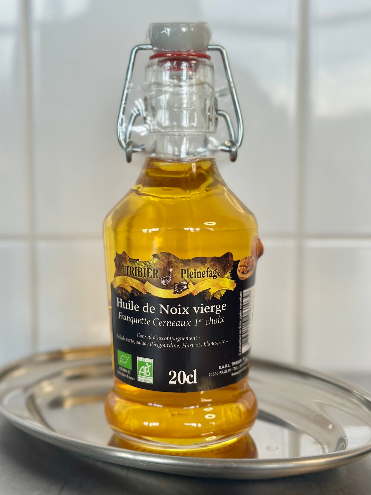 Bottle of walnut oil on a metallic tray with a white tiled background