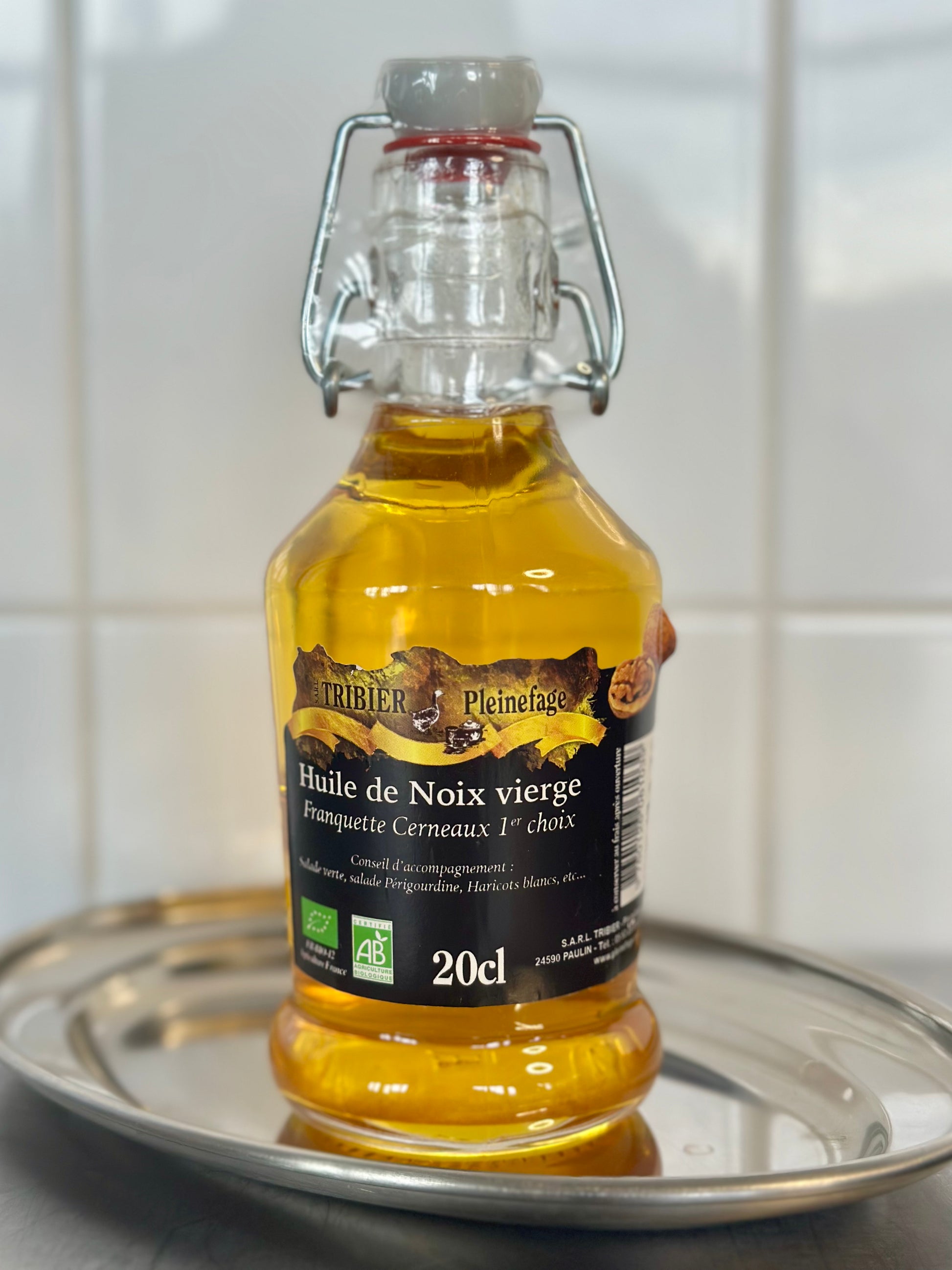 Bottle of walnut oil on a metallic tray with a white tiled background